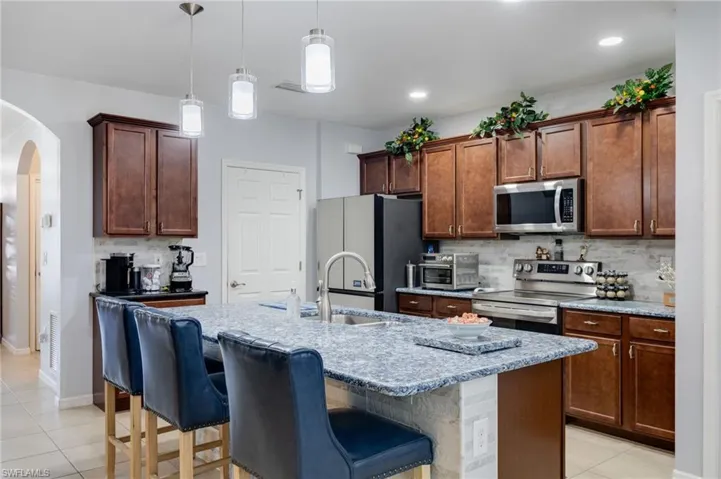 Kitchen featuring decorative backsplash, arched walkways, light tile patterned floors, a kitchen bar, and stainless steel appliances