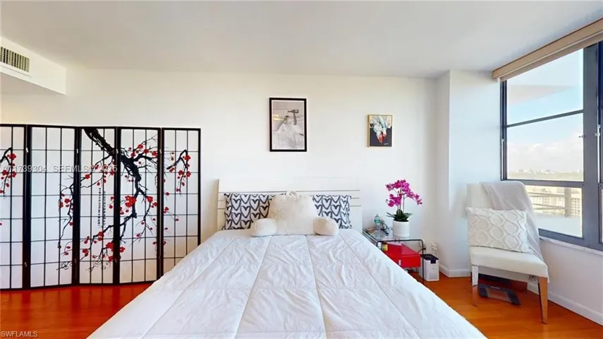 Bright interior space featuring a large window with city architecture visible, wood-finish flooring, and a white ceiling