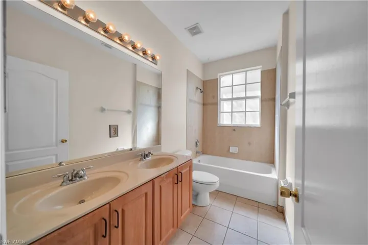 Bathroom with double vanity, shower / tub combination, and light tile patterned flooring