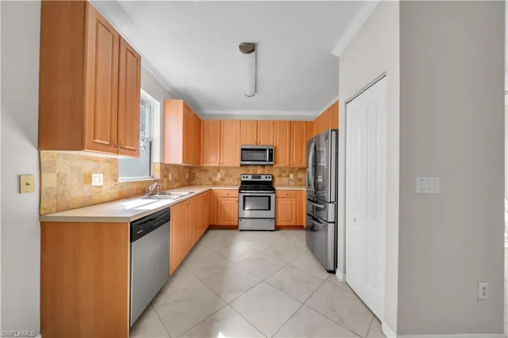 Kitchen with crown molding, light countertops, stainless steel appliances, light tile patterned floors, and backsplash