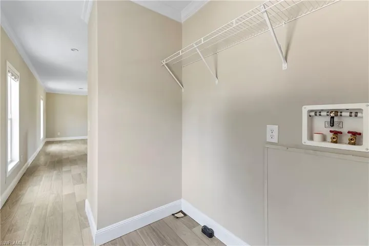 Laundry room featuring hookup for a washing machine, crown molding, a wealth of natural light, and wood-type flooring