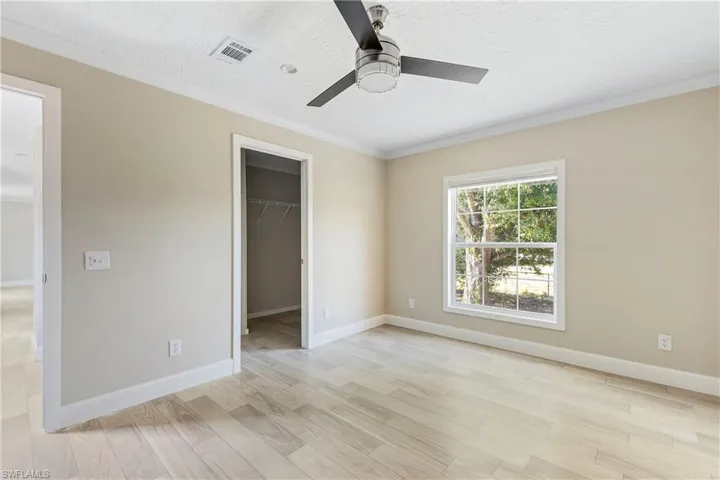 Main bedroom with ceiling fan, a closet, a walk in closet, and ornamental molding