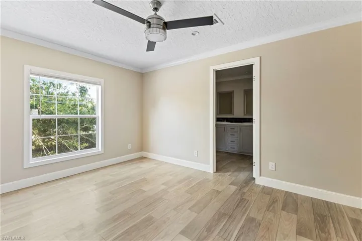 Main bedroom featuring ceiling fan, light wood-type flooring, a textured ceiling, ornamental molding, and a walk in closet