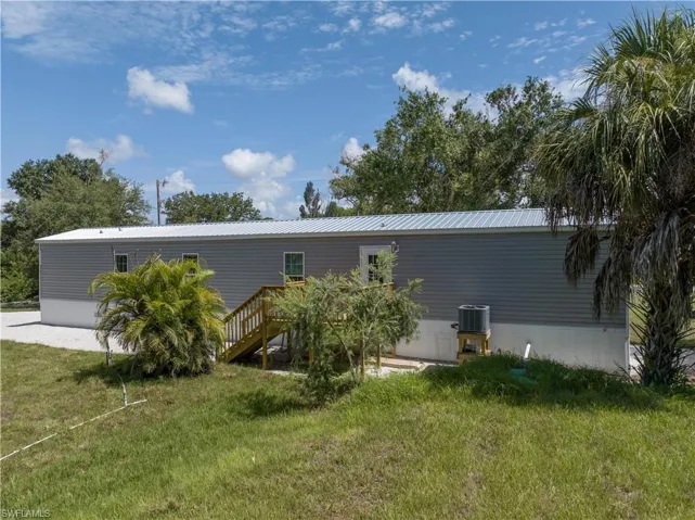 Back of property with central AC unit and a lawn
