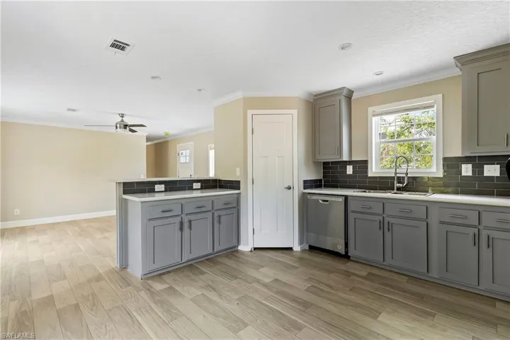 Kitchen featuring gray cabinetry, stainless steel dishwasher, backsplash, sink, and ceiling fan