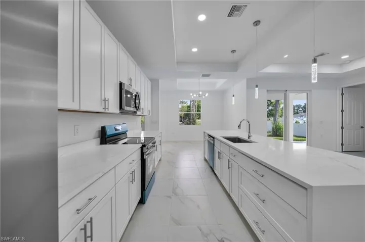 Kitchen with a raised ceiling, appliances with stainless steel finishes, white cabinets, light stone counters, and pendant lighting