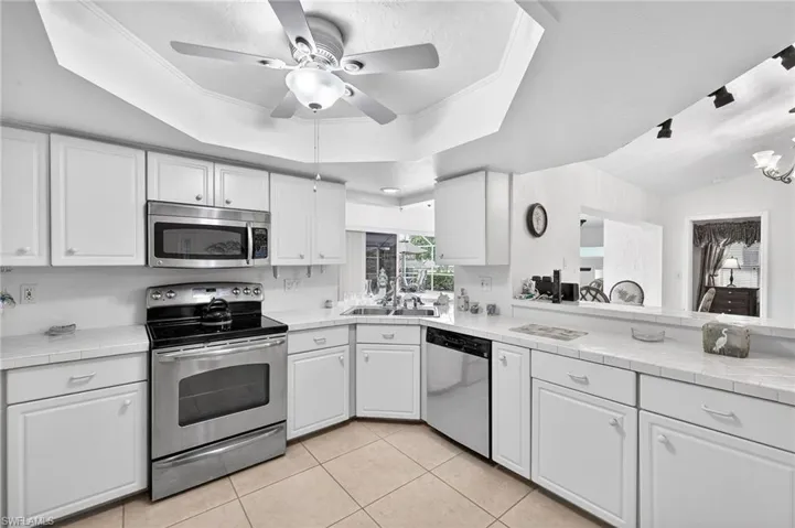 Kitchen with tile counters, stainless steel appliances, white cabinetry, crown molding, and a tray ceiling