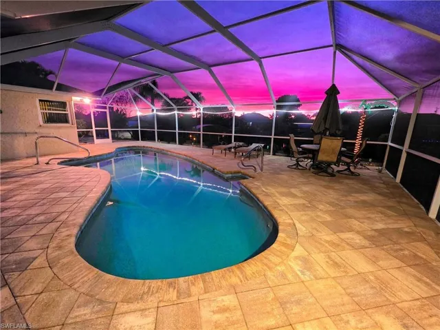 Pool at dusk with an outdoor pool, a lanai, a sunroom, and outdoor dining area
