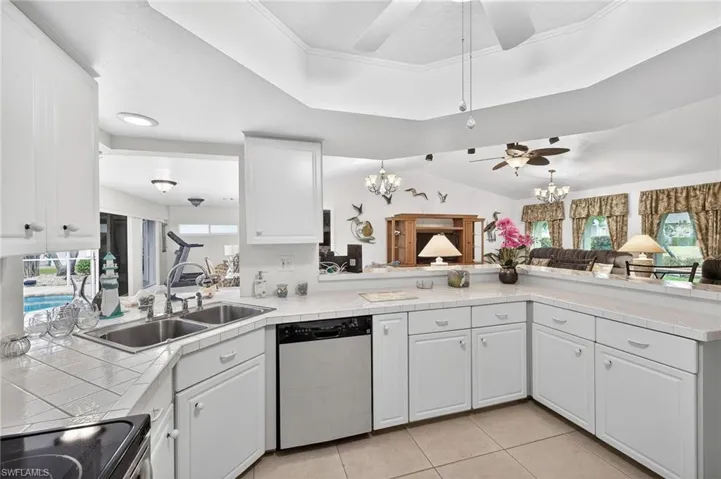 Kitchen featuring tile countertops, a chandelier, stainless steel dishwasher, black electric range, and vaulted ceiling