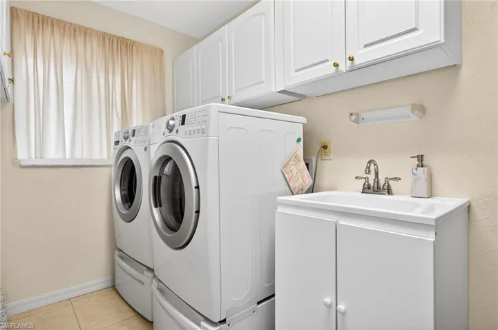 Laundry room with cabinet space, independent washer and dryer, a textured wall, and light tile patterned floors