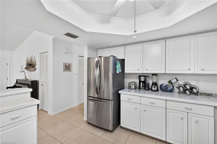 Kitchen featuring tile counters, freestanding refrigerator, a tray ceiling, ceiling fan, and white cabinetry