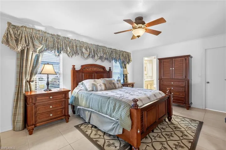 Bedroom featuring light tile patterned flooring, ceiling fan, and ensuite bathroom