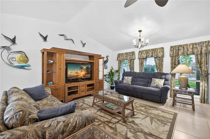 Living room featuring vaulted ceiling, ceiling fan, hanging lights, and light tile patterned flooring