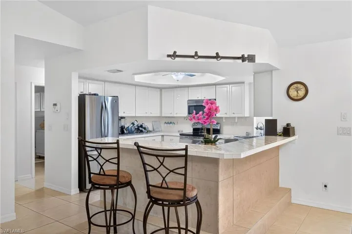 Kitchen featuring a breakfast bar, a peninsula, tile countertops, stainless steel appliances, and white cabinets
