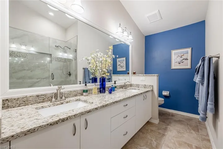 Full bath featuring toilet, a stall shower, double vanity, and a sink