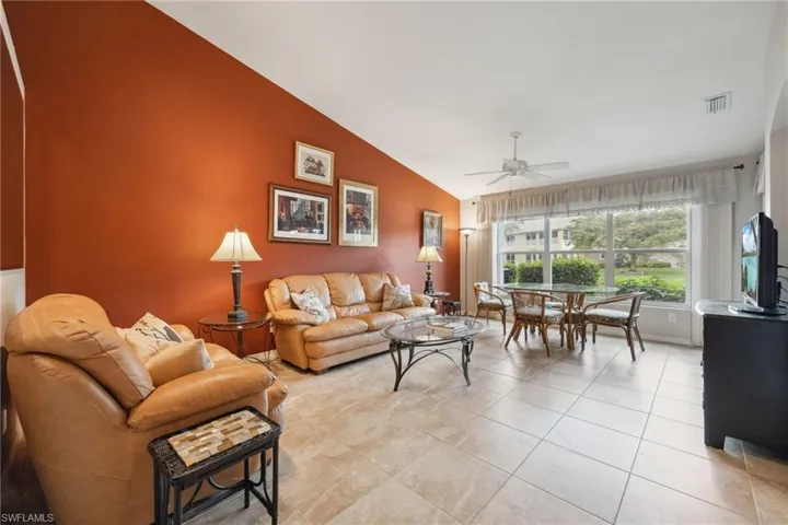 Living room with high vaulted ceiling, light tile patterned floors, visible vents, and a ceiling fan