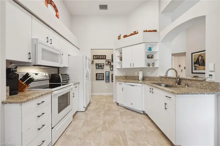 Kitchen featuring white appliances, open shelves, white cabinets, a high ceiling, and a sink