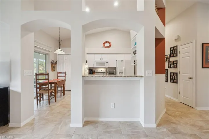 Kitchen with white cabinets, arched walkways, white appliances, a toaster, and light stone counters