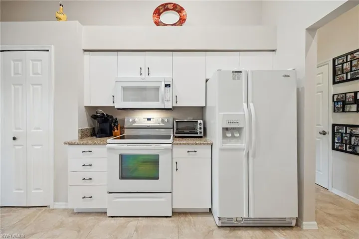 Kitchen featuring baseboards, white appliances, white cabinetry, light stone countertops, and a toaster