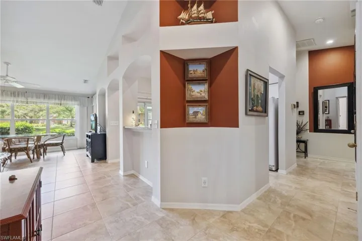 Corridor featuring baseboards, light tile patterned floors, a high ceiling, visible vents, and arched walkways