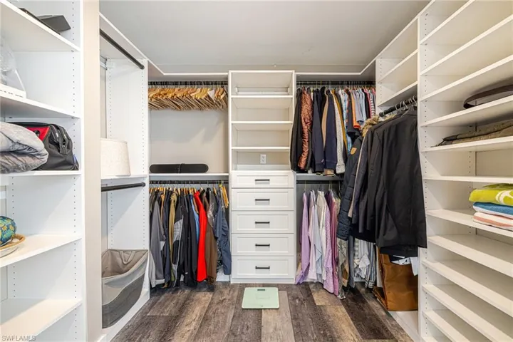 Walk-in closet featuring extensive white shelving, multiple hanging rods, five built-in drawers with dark hardware, and wood-finish flooring