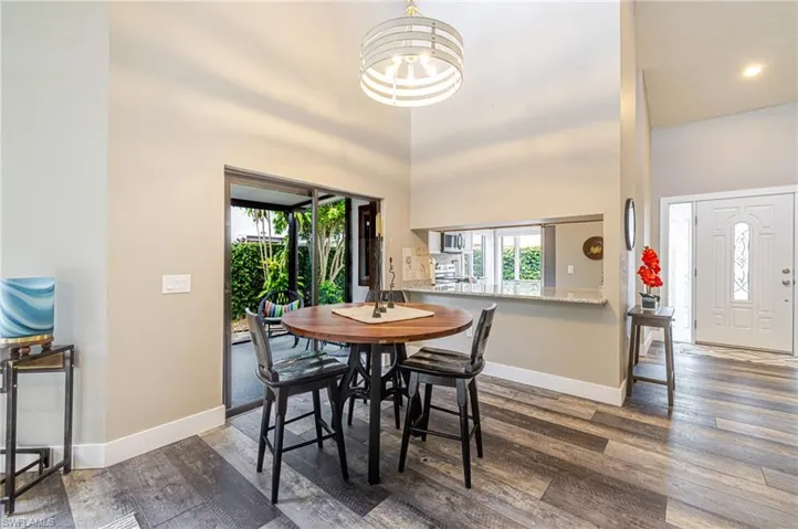 Wood-finish flooring throughout, featuring a pass-through kitchen opening, vaulted ceilings, and a decorative front entry door with side light