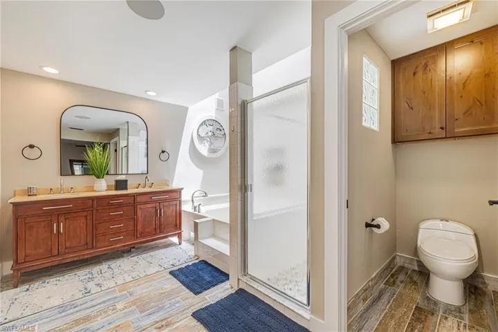 Bathroom featuring a double vanity with stone countertop, large arched mirror, enclosed shower, and a built-in bathtub