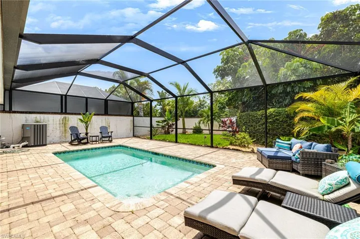 Screened outdoor pool area featuring a rectangular pool, paver deck, and lush tropical landscaping