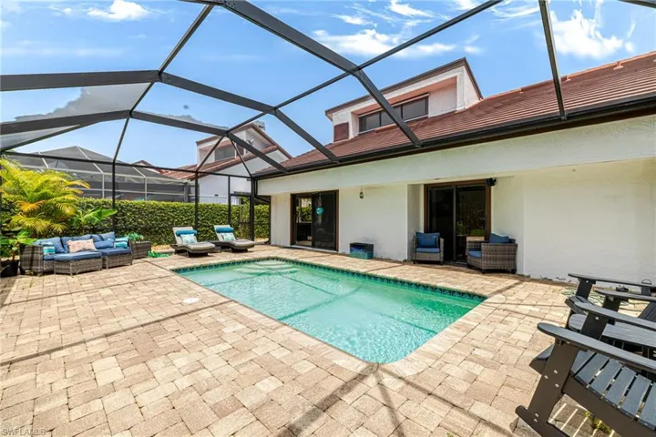 Screened-in outdoor living space featuring a rectangular swimming pool with integrated steps, a paver patio, and mature perimeter landscaping