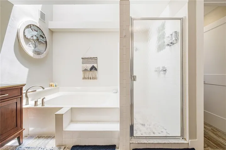 Bathroom featuring a built-in tub with tile surround and steps, a glass-enclosed shower with tile detailing, and wood-finish flooring
