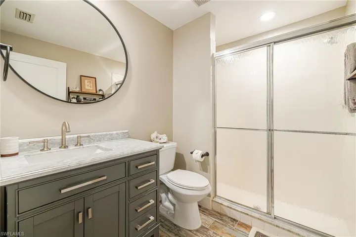 Bathroom featuring a gray vanity with an integrated sink, brushed nickel fixtures, a round wall mirror, and a shower with sliding frosted glass doors