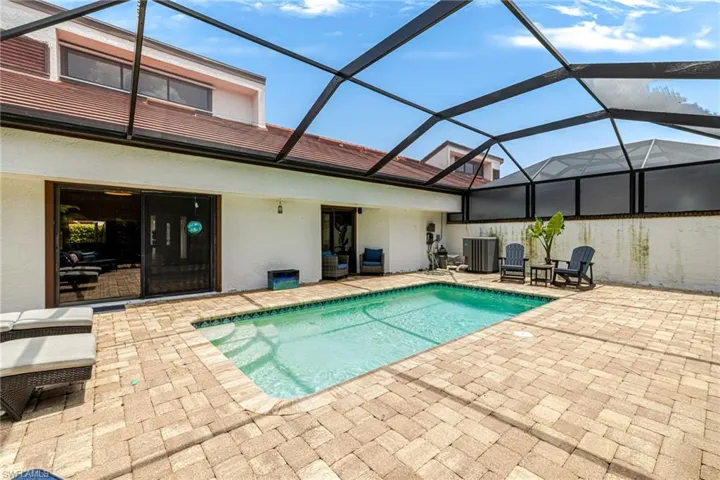Screened-in pool area featuring a rectangular swimming pool with integrated steps, surrounded by extensive paver decking