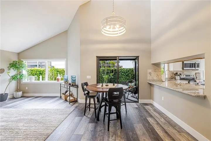 Open concept living area featuring vaulted ceilings, wood-finish flooring, and a dining space with a modern drum pendant light