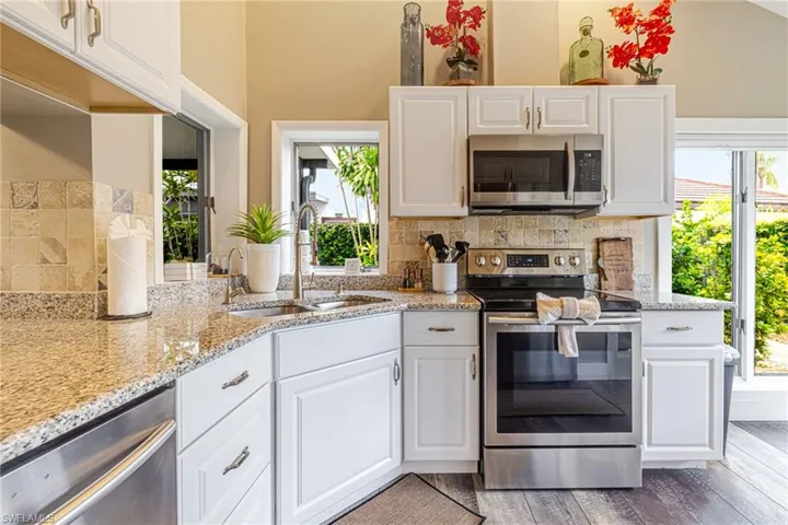 Kitchen featuring granite countertops, white cabinetry with decorative hardware, stainless steel appliances, a tile backsplash, and wood-finish flooring