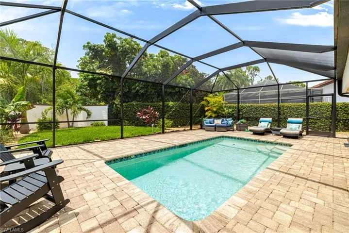 Screened outdoor living area featuring a rectangular pool with integrated steps, surrounded by paver decking, and a privacy hedge