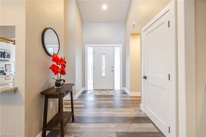 Entryway featuring wood-finish flooring, a white paneled door with black hardware, and a white front door with decorative glass inserts