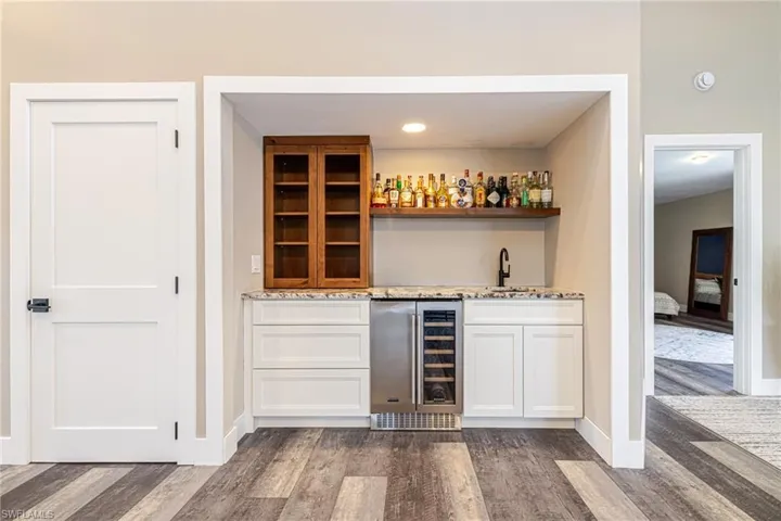 Built-in wet bar featuring a beverage cooler, single basin sink with a matte black faucet, and a floating wood shelf