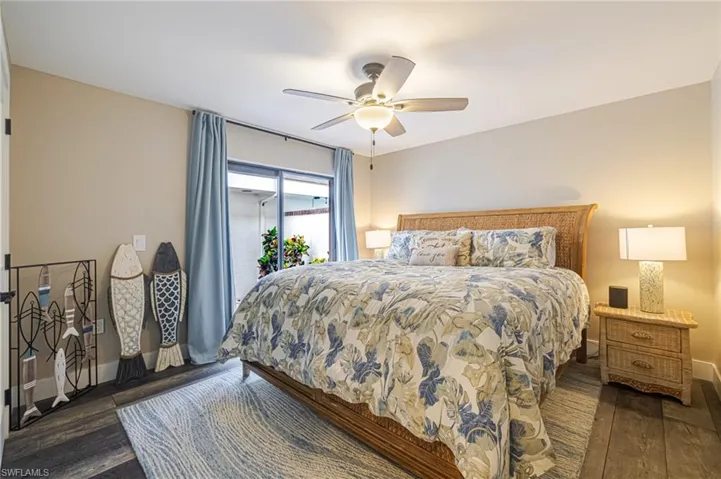Spacious bedroom featuring wood-finish flooring, a ceiling fan with integrated lighting, and a sliding glass door providing outdoor access