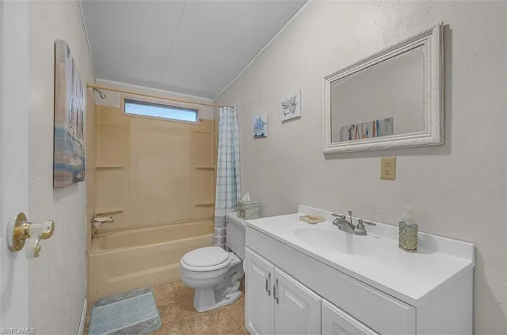 Full bath featuring a textured wall, vanity, shower / bathtub combination with curtain, and light tile patterned floors