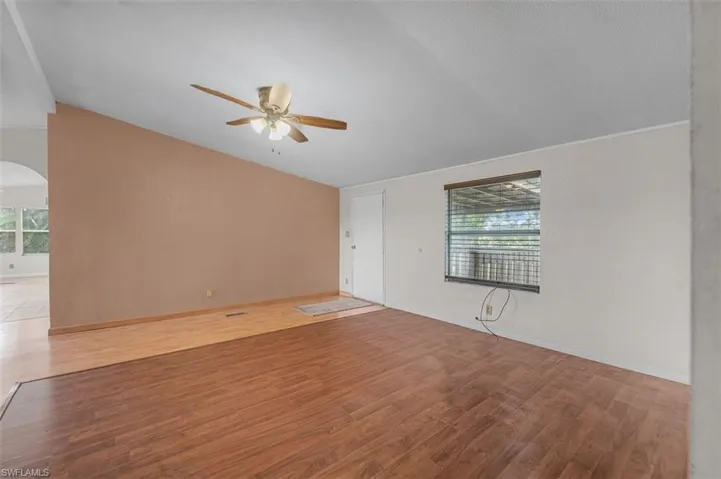 Spare room featuring light wood-style flooring, ceiling fan, arched walkways, and vaulted ceiling