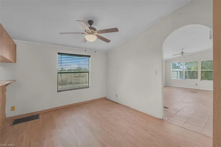 Unfurnished room featuring a ceiling fan, lofted ceiling, arched walkways, and light wood finished floors