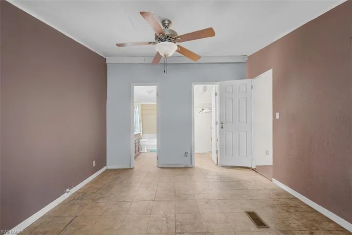 Unfurnished bedroom featuring ensuite bathroom, a walk in closet, ceiling fan, and crown molding