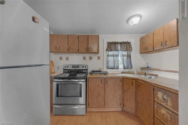 Kitchen featuring appliances with stainless steel finishes, light countertops, light wood-style floors, and brown cabinetry