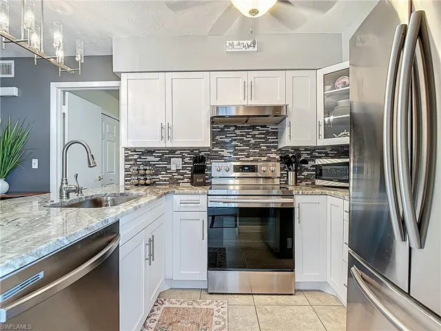 Kitchen featuring appliances with stainless steel finishes, backsplash, white cabinetry, light tile patterned flooring, and a textured ceiling