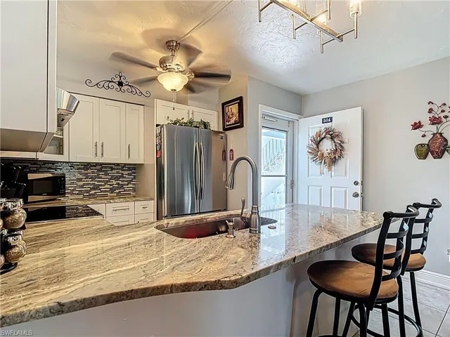 Kitchen featuring freestanding refrigerator, light stone countertops, decorative backsplash, white cabinetry, and a breakfast bar area