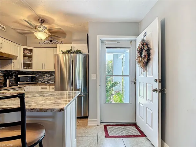 Kitchen with appliances with stainless steel finishes, light tile patterned floors, glass insert cabinets, white cabinets, and decorative backsplash