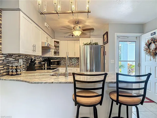 Kitchen featuring a peninsula, stainless steel appliances, a ceiling fan, tasteful backsplash, and glass insert cabinets