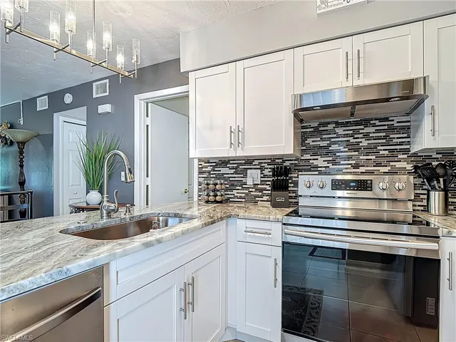 Kitchen with appliances with stainless steel finishes, under cabinet range hood, white cabinetry, light stone counters, and decorative backsplash