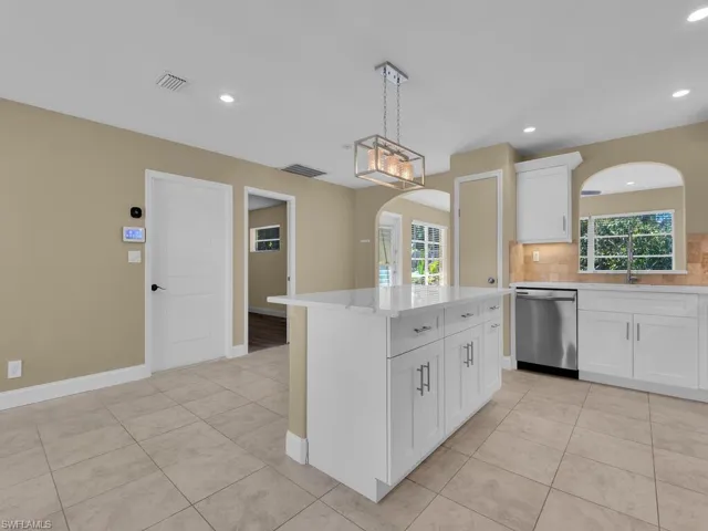 Kitchen featuring light tile patterned flooring, visible vents, arched walkways, stainless steel dishwasher, and backsplash