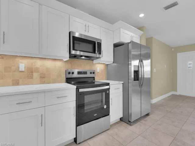 Kitchen featuring decorative backsplash, light tile patterned flooring, visible vents, stainless steel appliances, and white cabinetry